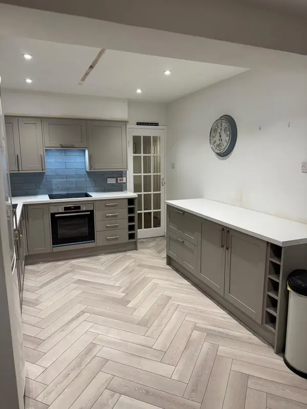 Renovated kitchen with grey units, white worktops and herringbone floor