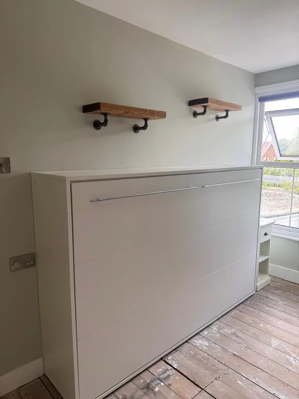 Wall bed folded into its cabinet under wall shelves